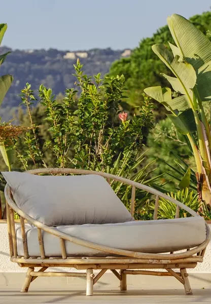 Piscina moderna con tumbonas blancas junto a un jardín verde exuberante y una vista despejada hacia el horizonte.