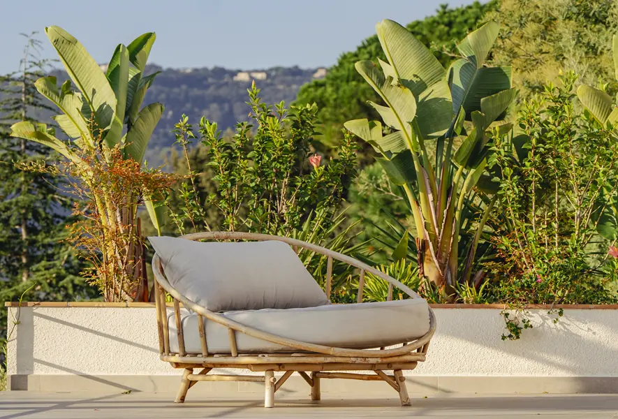Piscina moderna con tumbonas blancas junto a un jardín verde exuberante y una vista despejada hacia el horizonte.